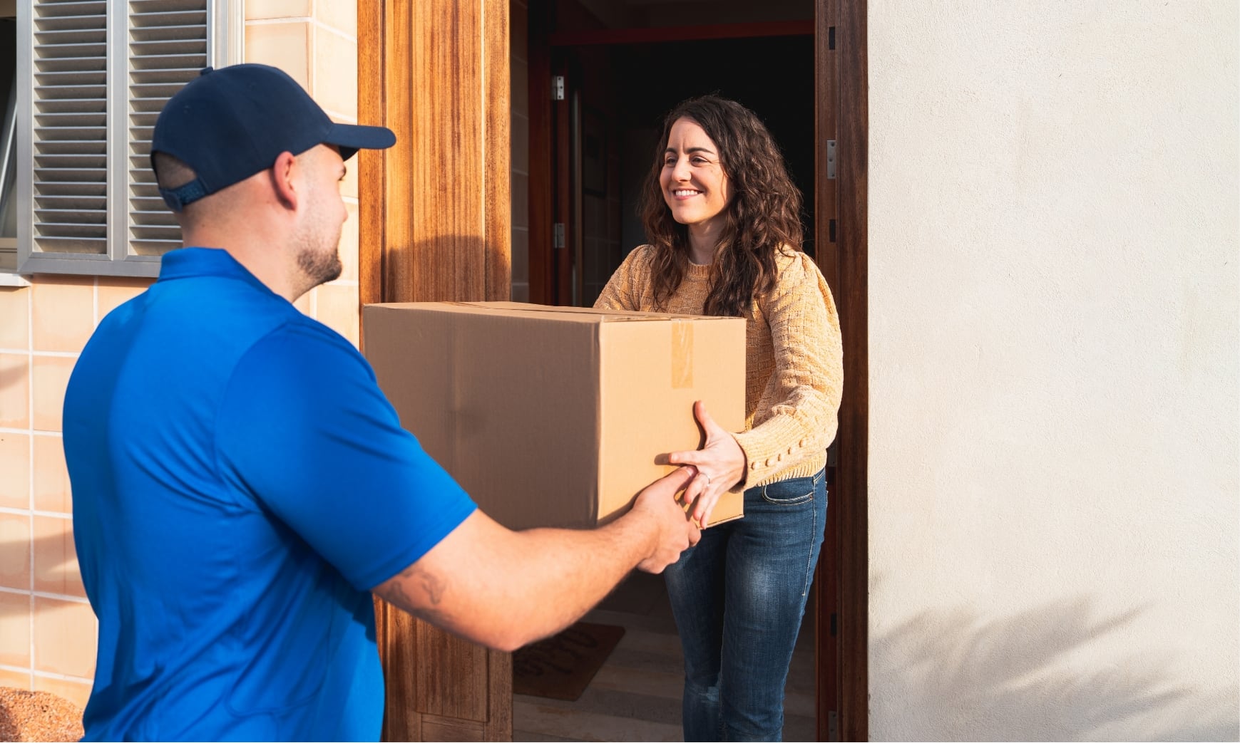 Un livreur donne un colis à une femme devant son domicile.