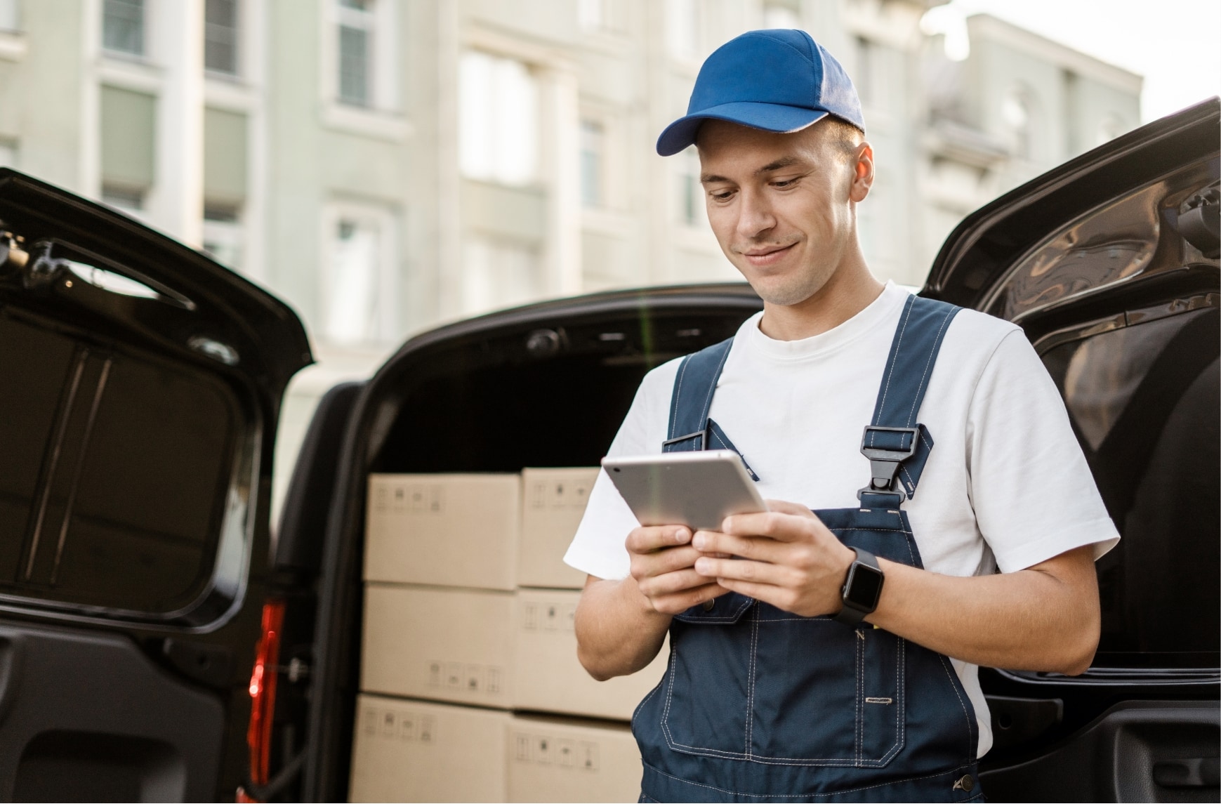 Un livreur est devant un camion chargé avec des colis et utilise une tablette.