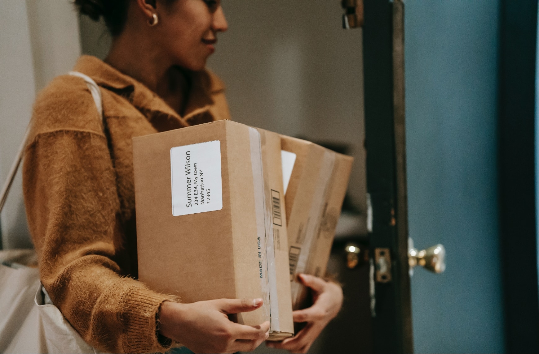 Une femme qui se trouve dans l'entrée d'un appartement porte deux colis.