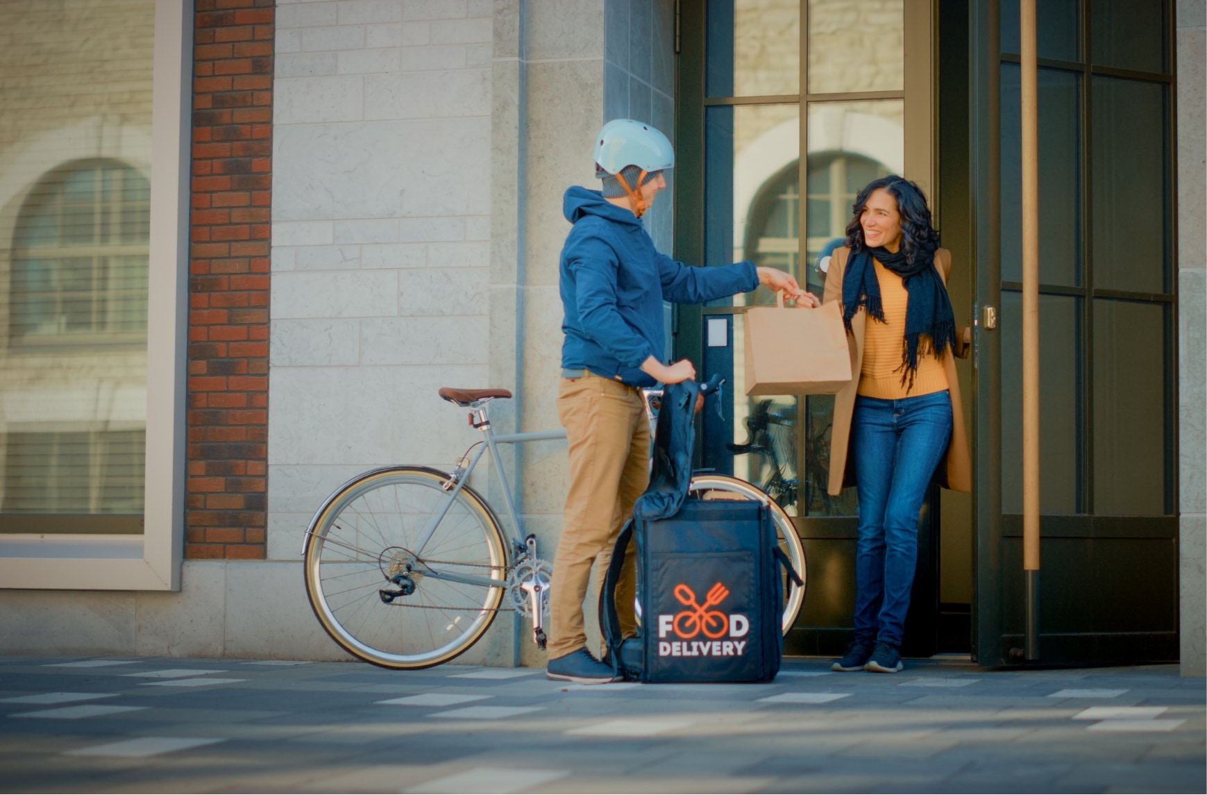 Un livreur à vélo donne un repas à une femme devant son domicile.