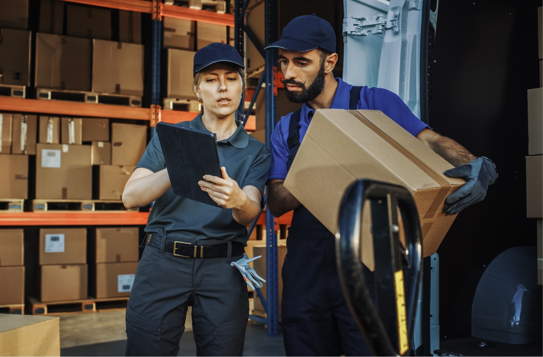 Two people in front of a warehouse use software to dispatch transport operations.