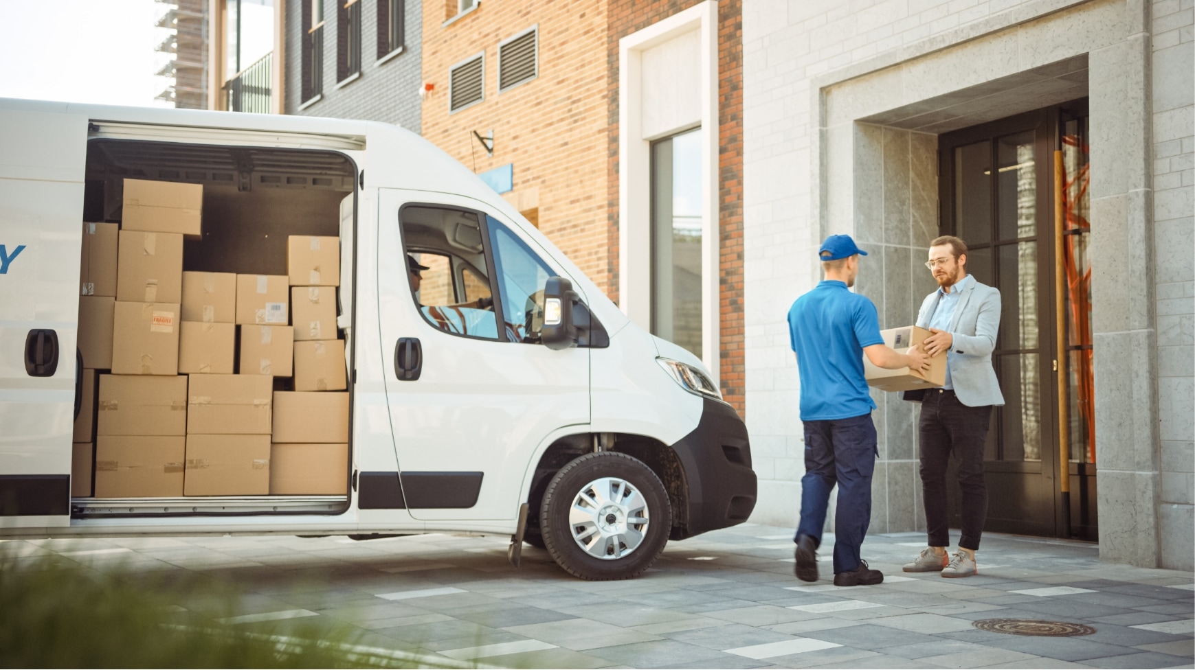 A deliveryman gives two parcels to a man in front of his building.