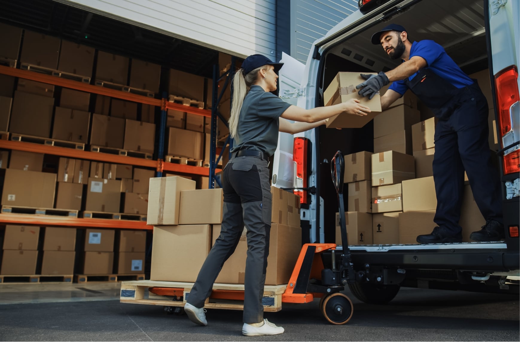 Two delivery drivers loading parcels in a warehouse near a town.